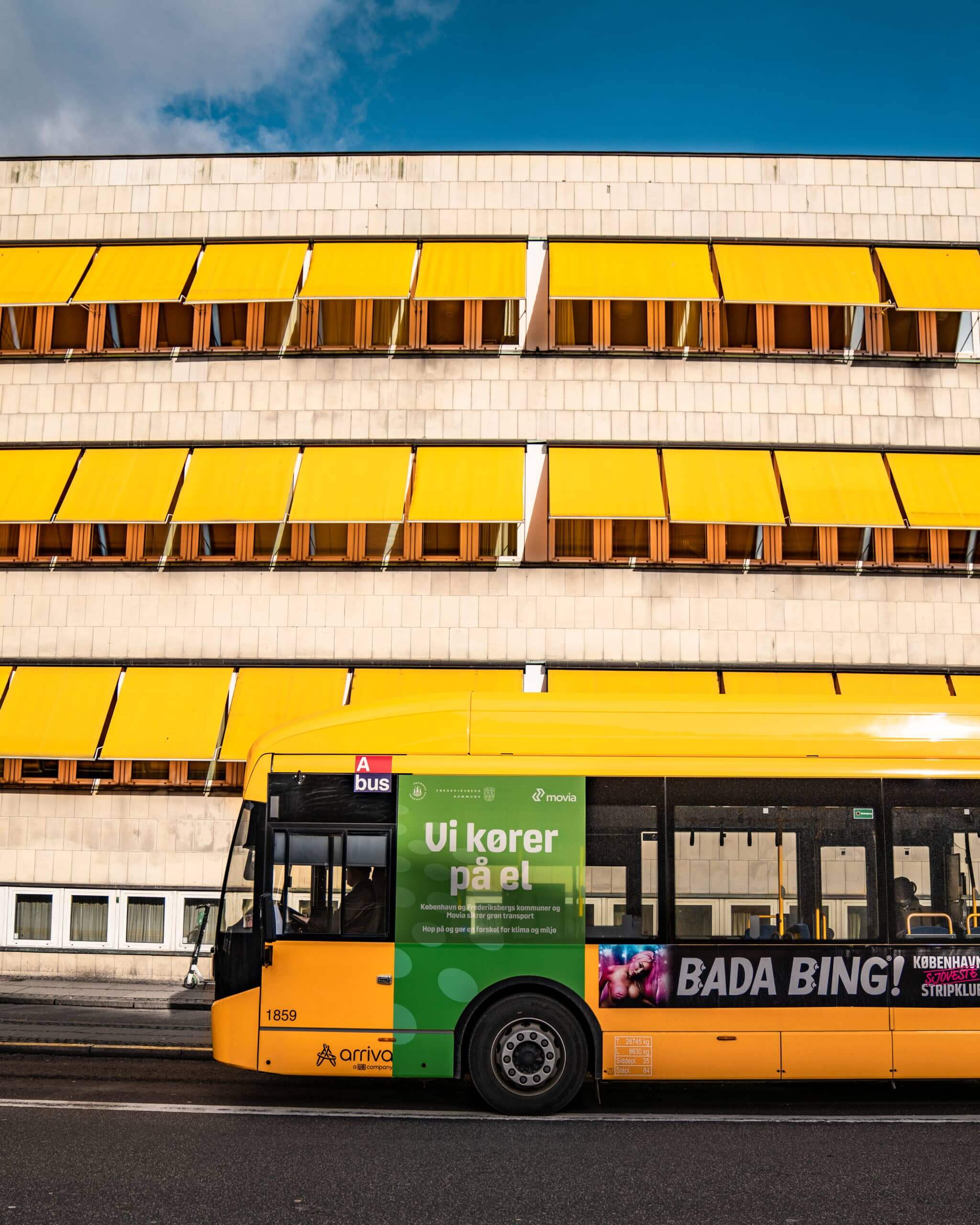 Ein gelber Bus vor einem Gebäude mit gelben Markisen.