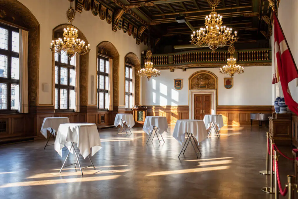 Rathaus Kopenhagen Ein Raum mit Tischen und Kronleuchtern.